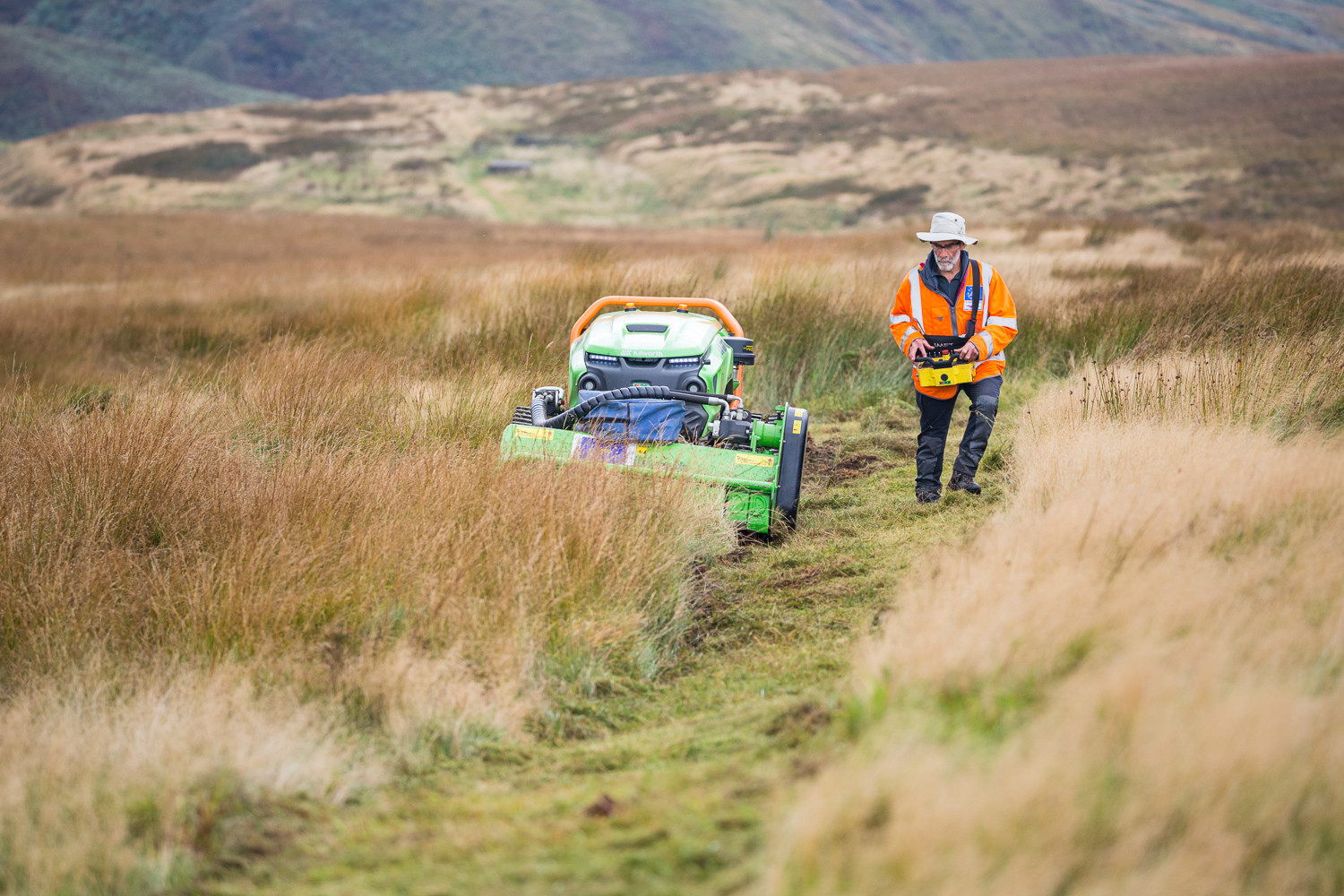 man in high vis and safety helmet in the middle of a dry moor with a vehicle in the background