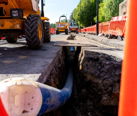 image of long blue pipe in the road with barriers and person in high vis in the distance