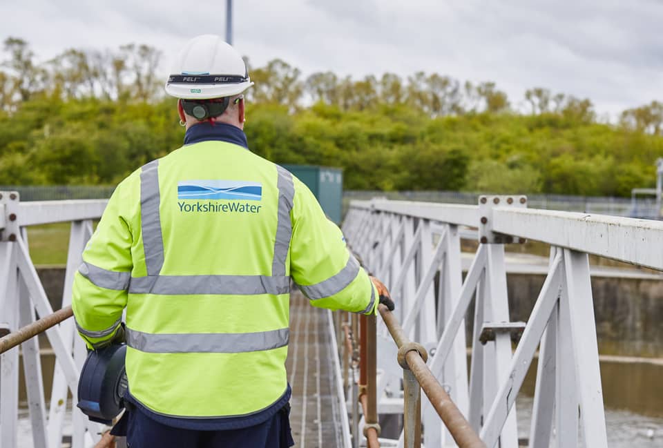 A Yorkshire Water employee wearing a high-vis jacket featuring the Yorkshire Water logo walks over a bridge