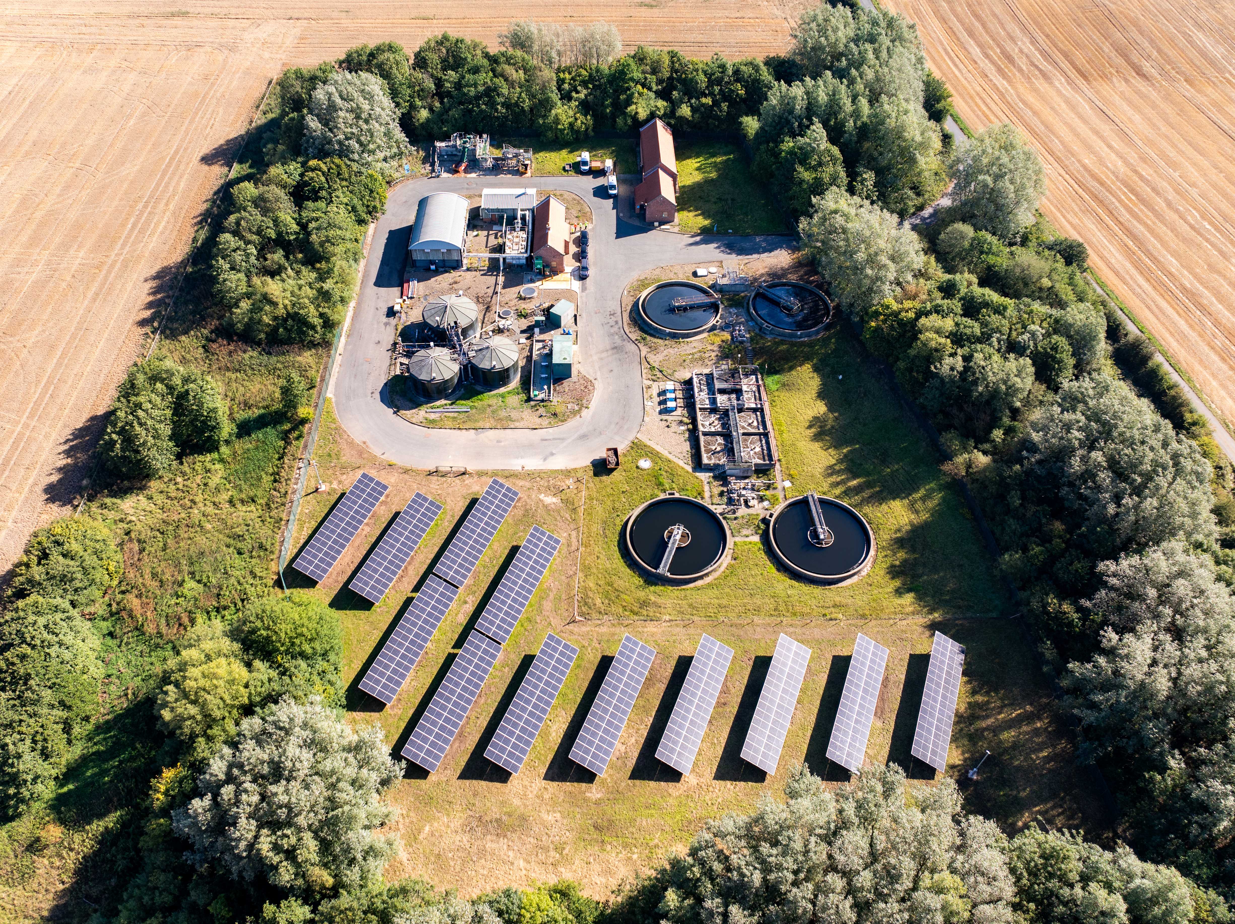 Aerial image of wastewater treatment site with tanks foliage and lots of solar panels