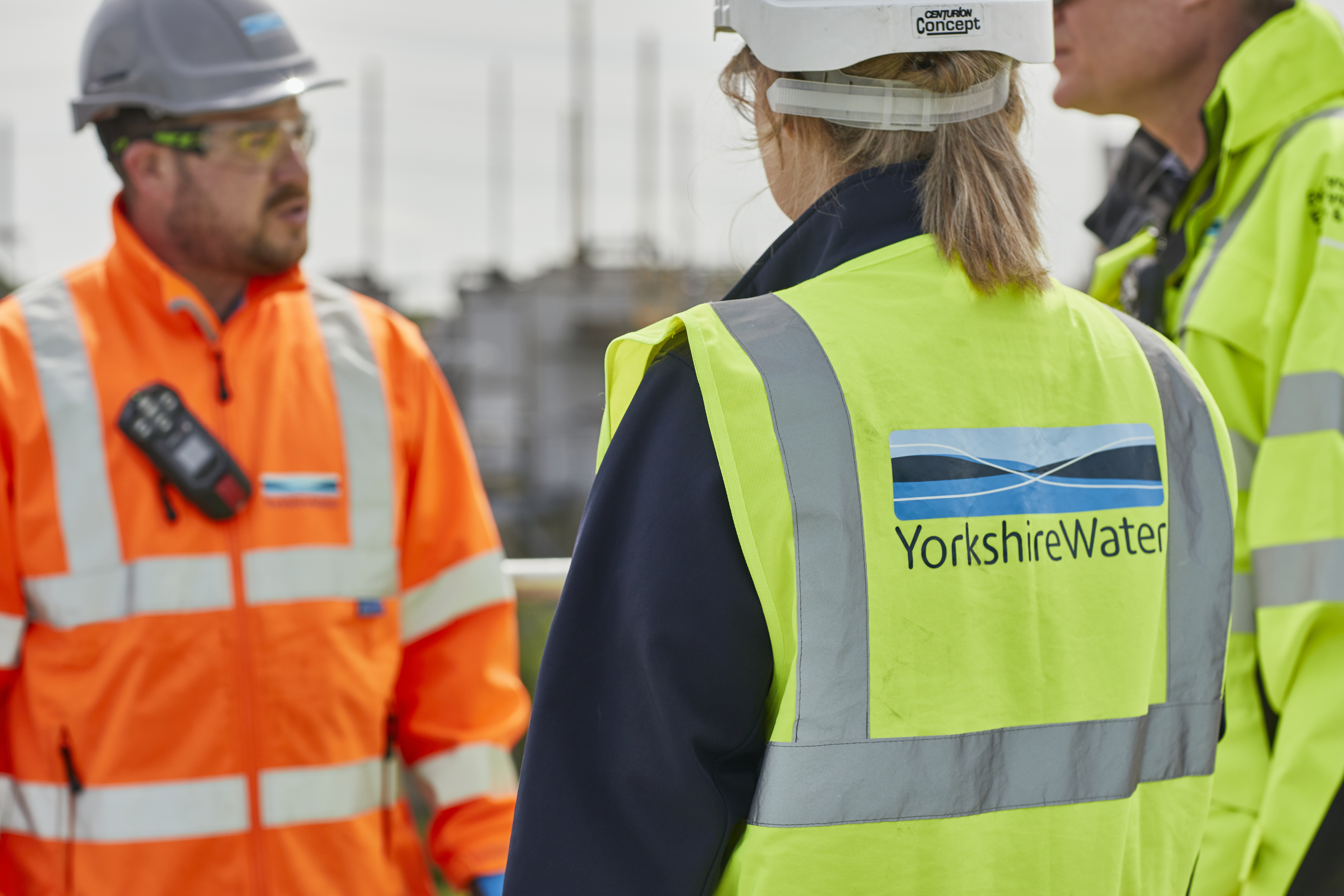 Three Yorkshire Water colleagues wearing high visibility jackets and helmets at a wastewater treatment works
