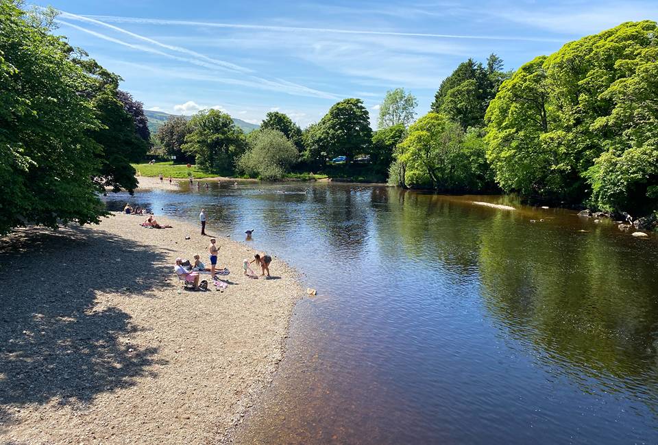 People on the riverbank of the river Wharfe in Ilkley at the bathing water on a sunny day