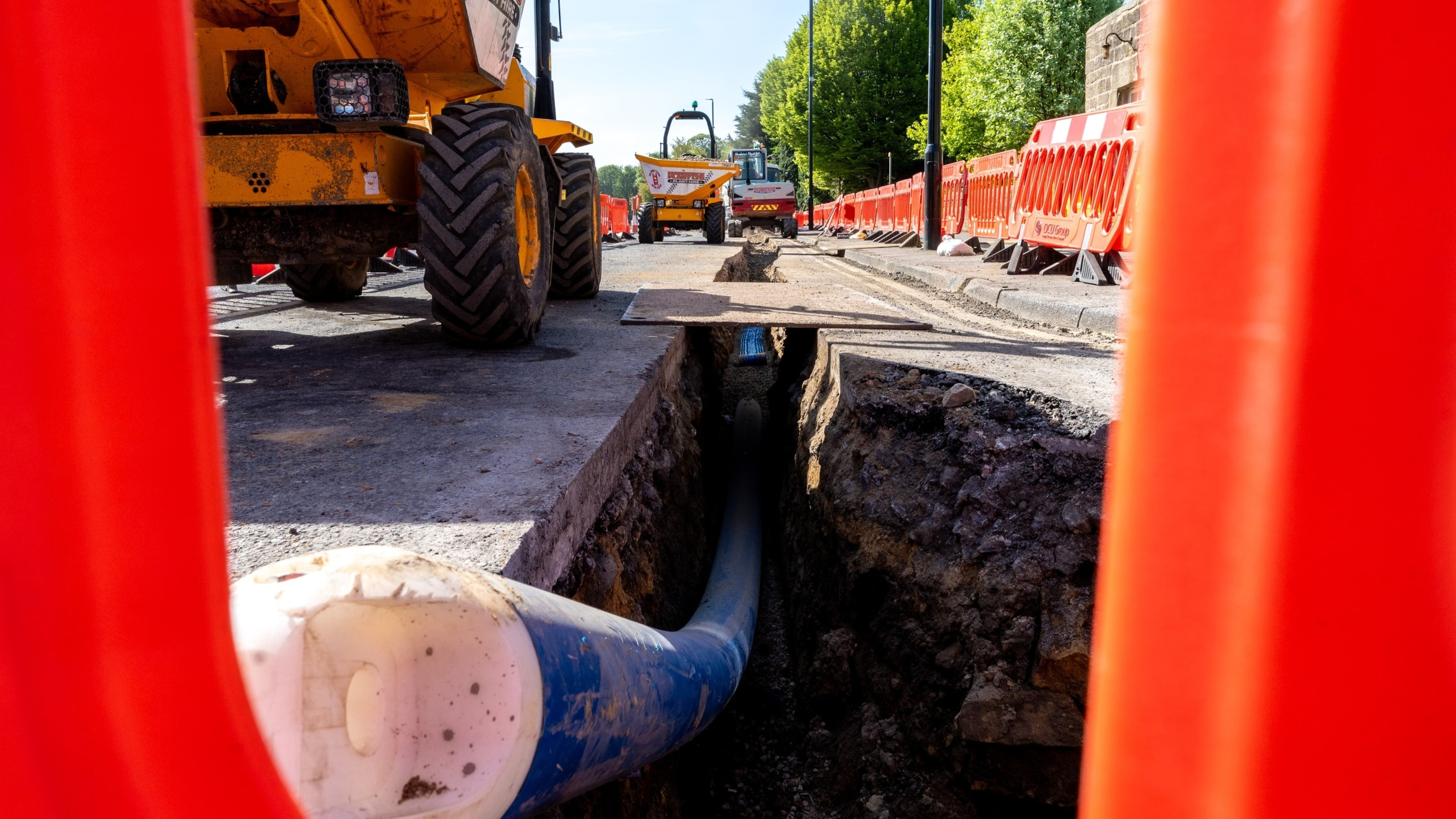 Blue pipe in trench on the road with worker in high vis in the background