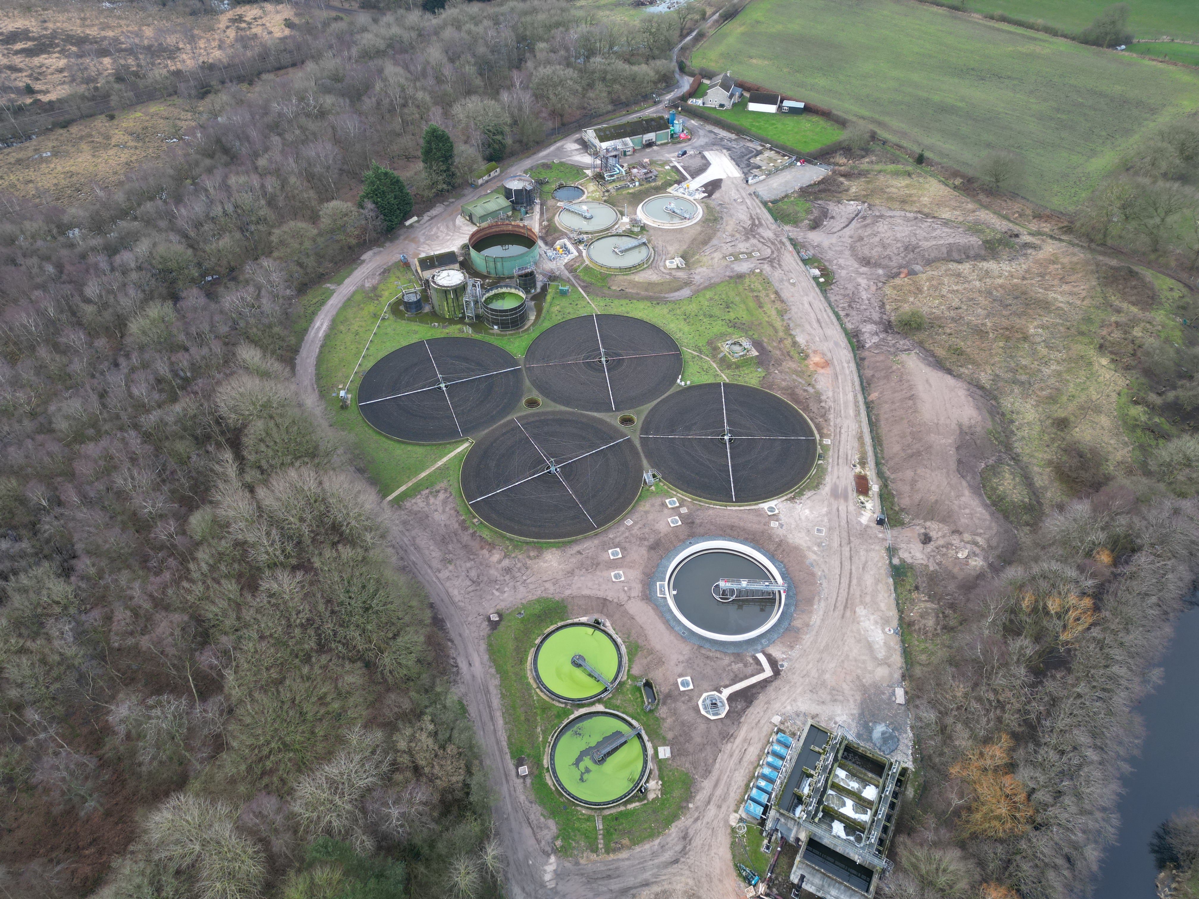aerial image of a wastewater treatment works with several round tanks surrounded by trees and greenery