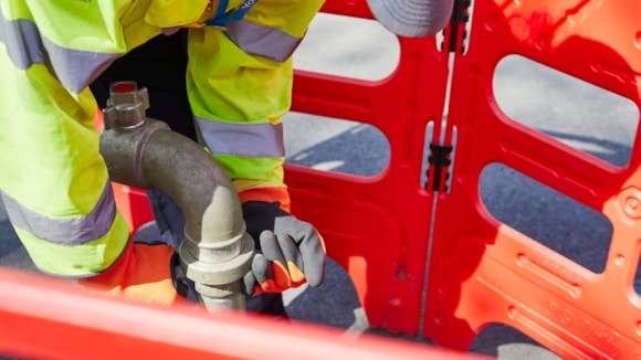 Close up of person in high vis behind orange safety barrier with pipe