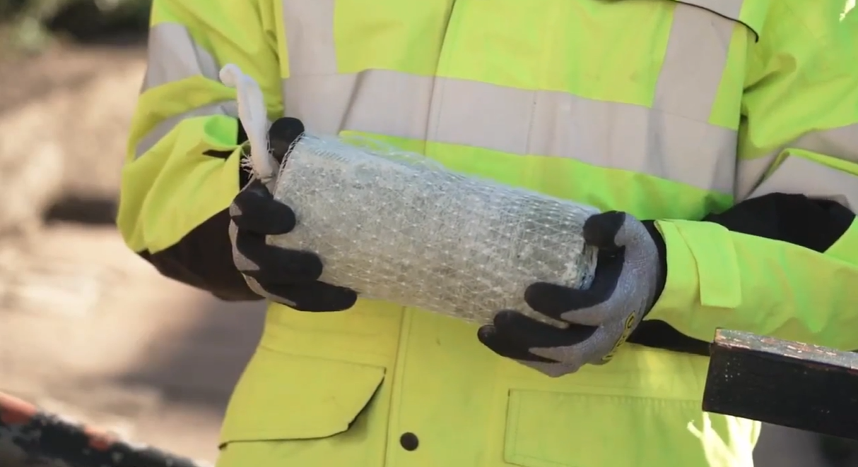waist height close up of person in high vis and gloves holding a cyndrical block encased in netting 