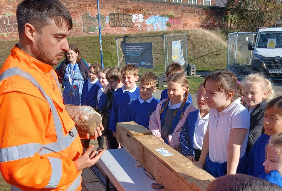 man in high vis jacket shows primary school children an old historic brick as part of a dig