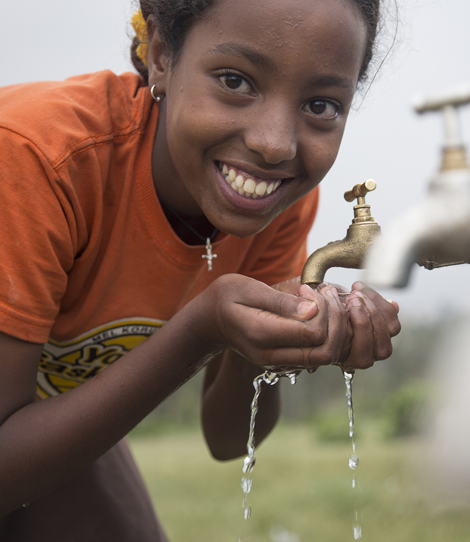 14 year old Mekedelawit Endrias, grade 7 pupil and WASH club member at the taps tasting the safe, clean water, at Bruh Tesfa Primary School, Addis Ababa, Ethiopia, 2013.