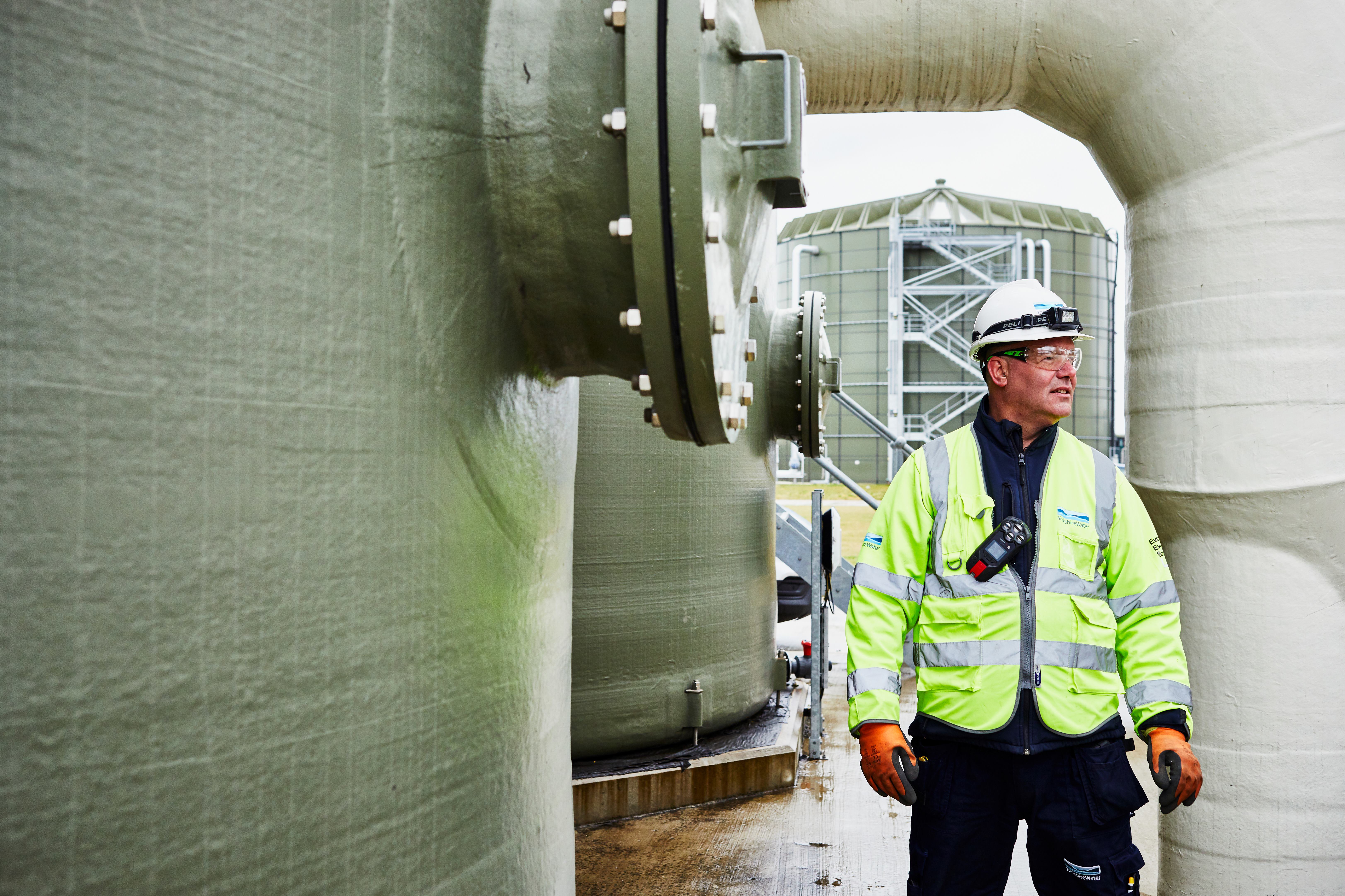man in high vis and hard hat stood beside a large storage tank