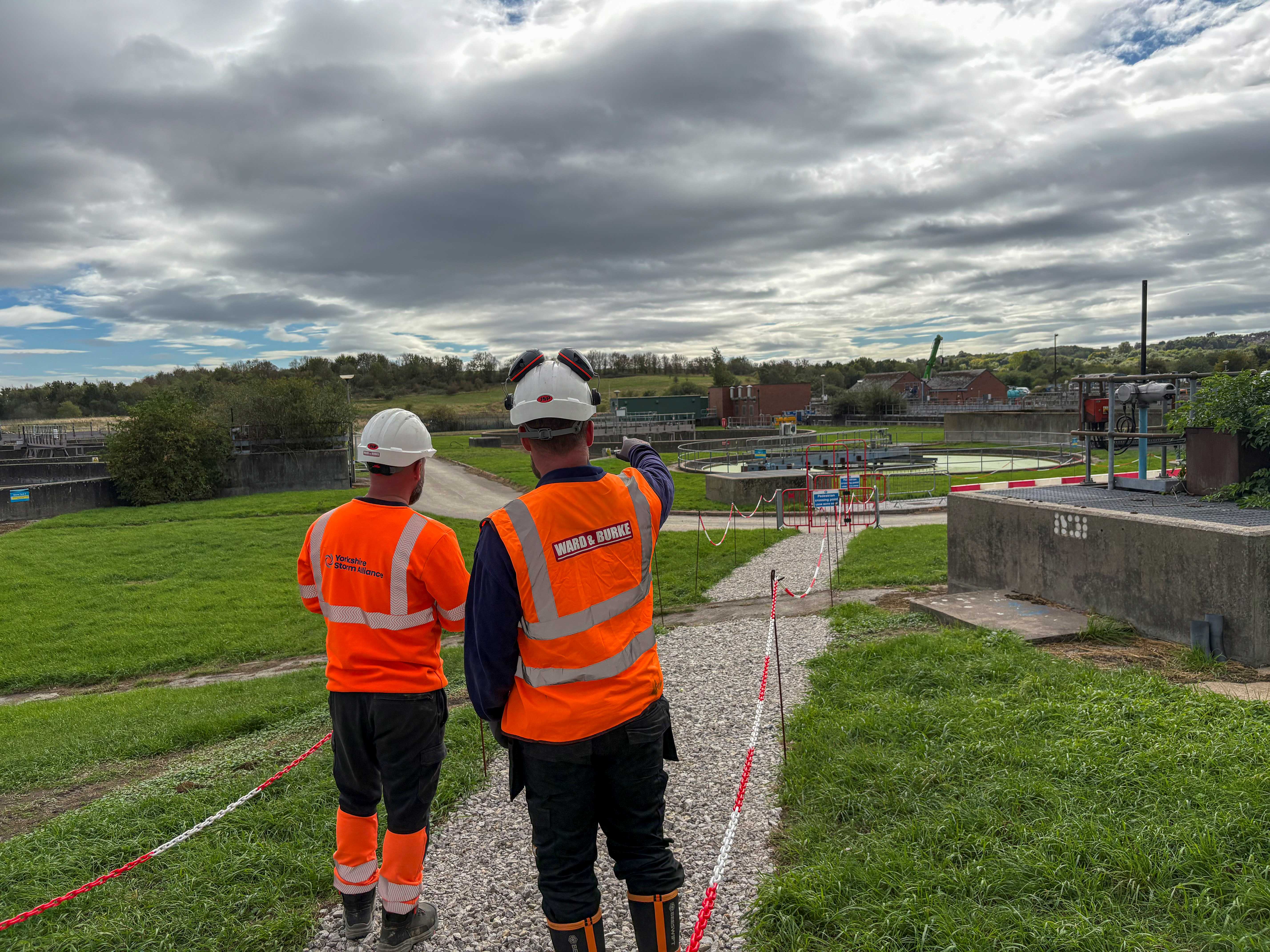 The back of two people in high vis and hard hats looking over a wastewater treatment site