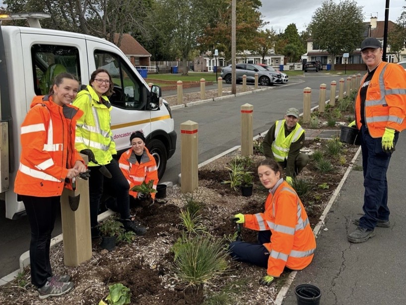 six people in high vis jackets planting in a central rain garden in a street