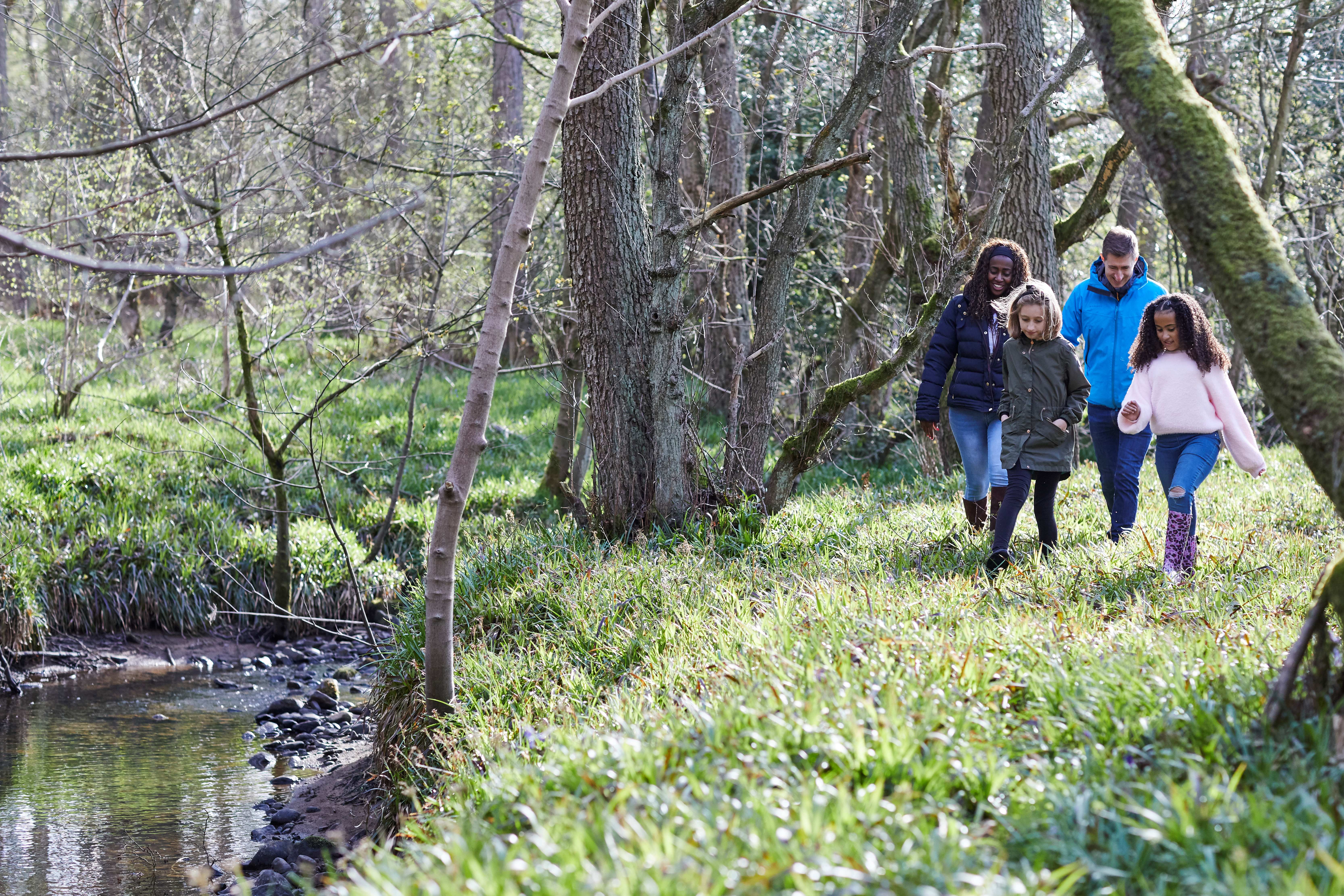 two adults and two children in warm outdoor wear walking through woodland