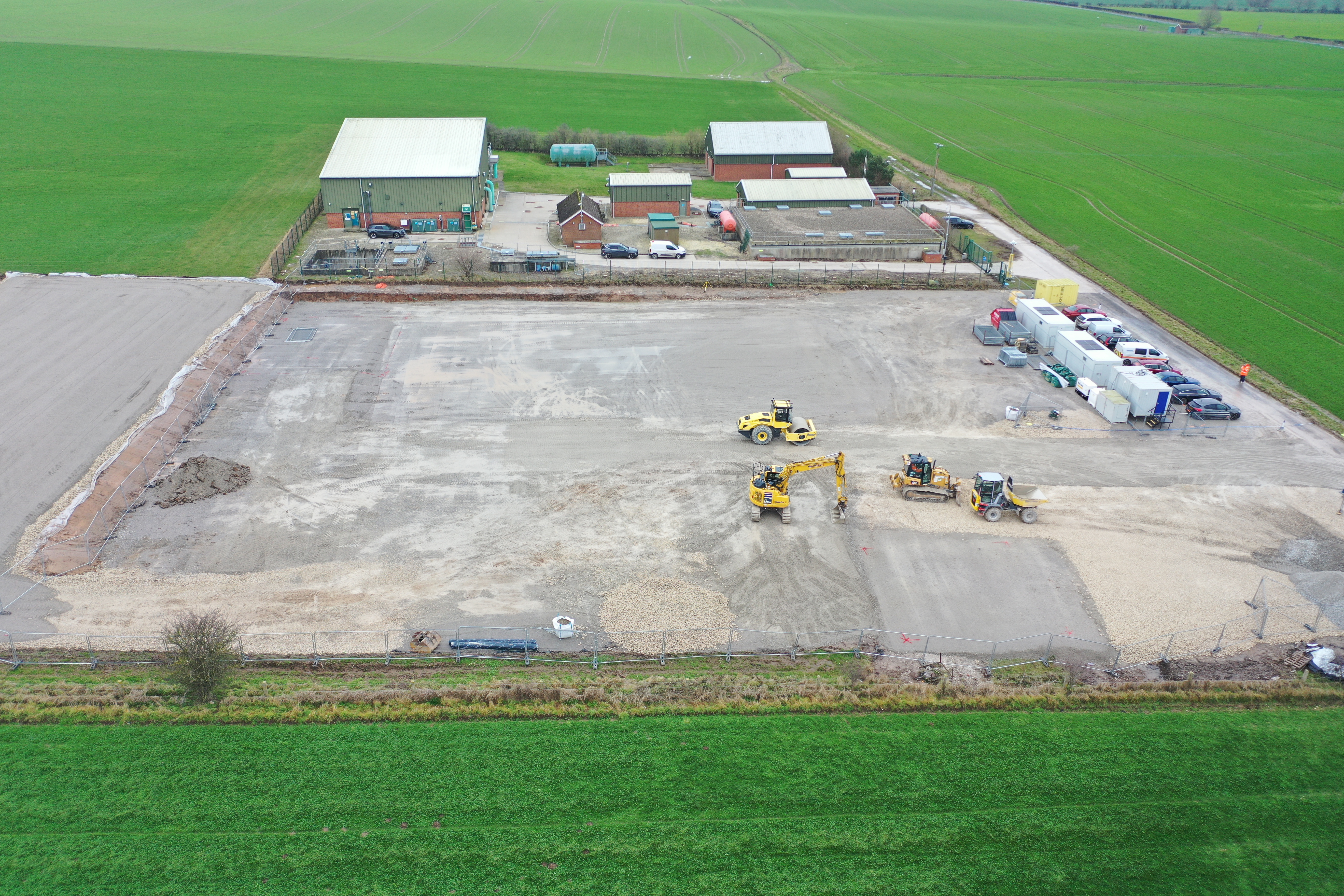 Aerial view of wastewater treatment plant with crane and vehicles on tarmac in green field