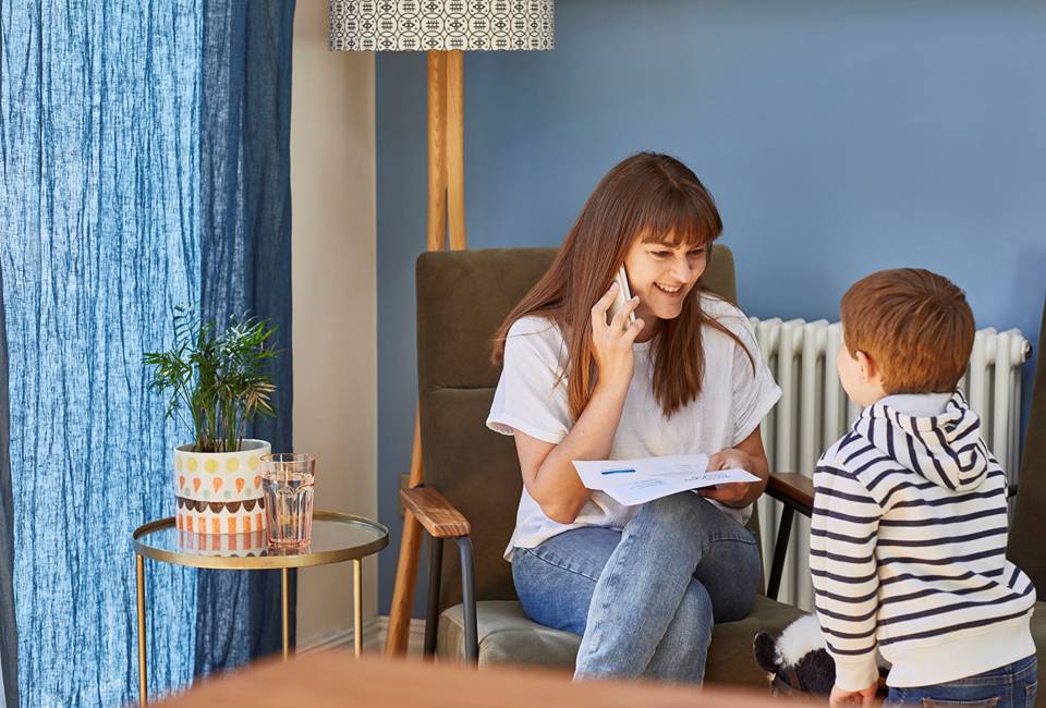 A woman sitting in chair on the phone while holding a letter from Yorkshire Water and smiling at a small child