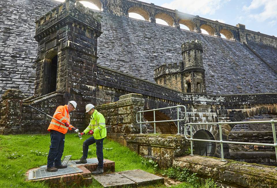 Yorkshire Water colleagues at Scarhouse reservoir taking a water sample with the dam in the background