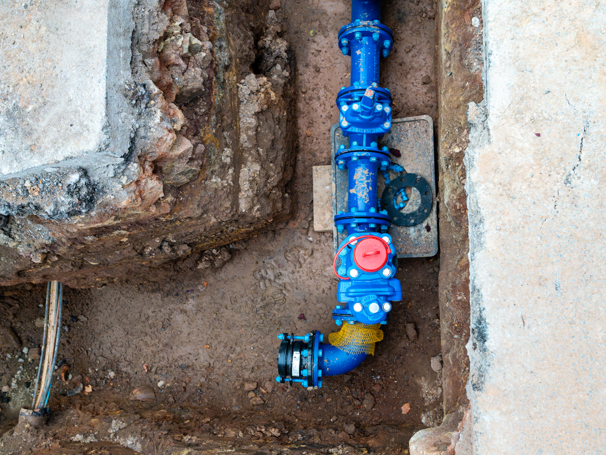 blue pipe in trench with orange road barriers around it and person in high-vis jacket in the background