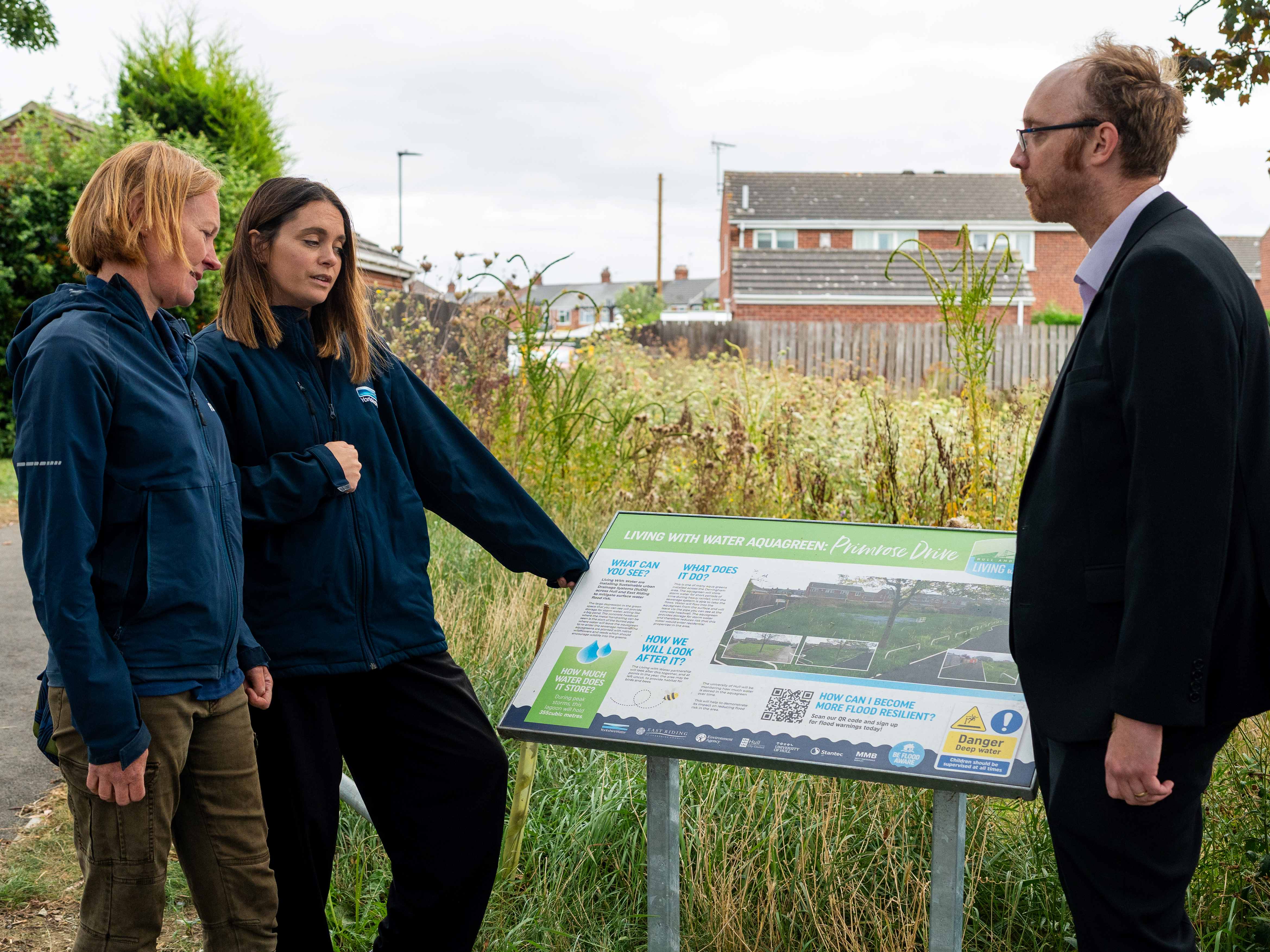 three people looking at an information board with meadow aquagreen in the background