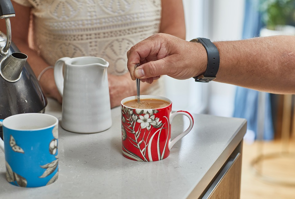 Two people making cups of tea in a red mug and a blue mug