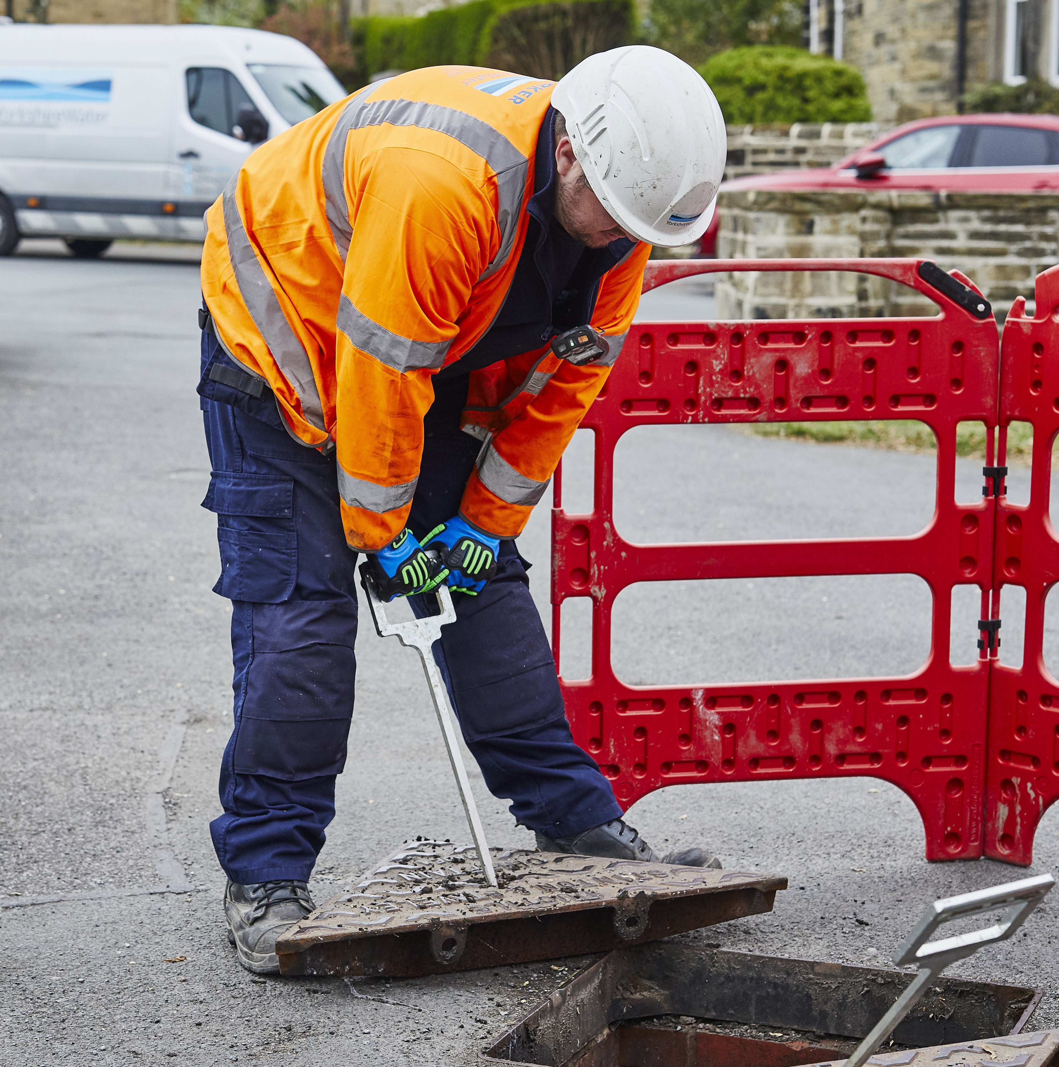 Person in high vis and hard hat removing a manhole cover on a road inside road safety barriers 
