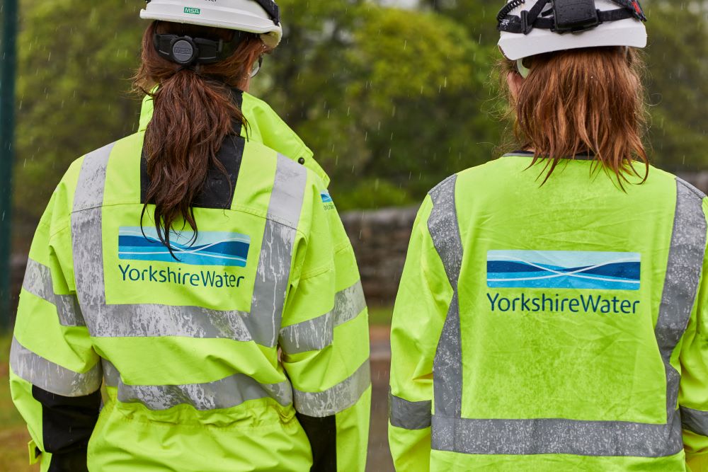 Two Yorkshire Water colleagues walking together in the rain with high visibility jackets and helmets on