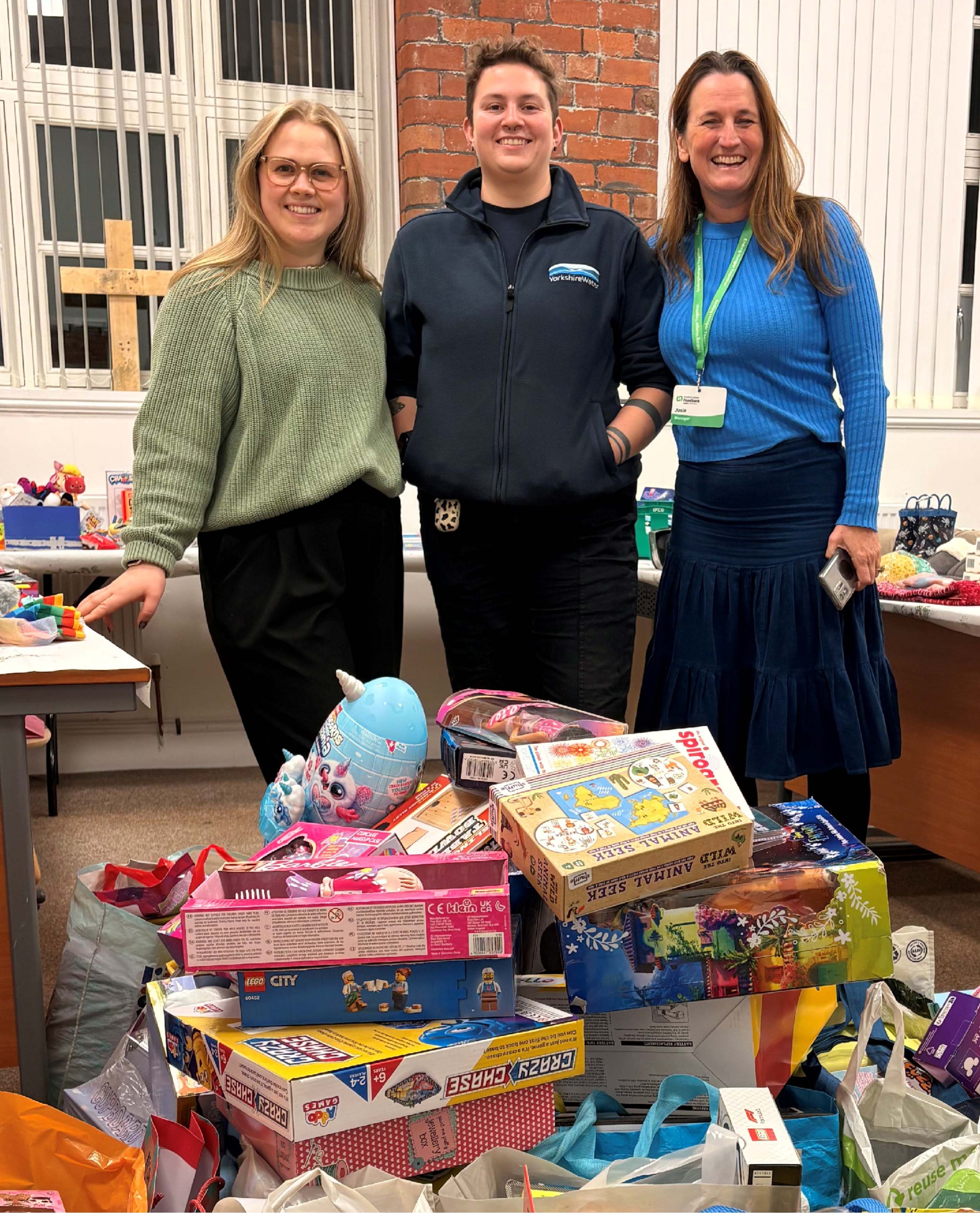 3 people smiling behind lots of children's presents 